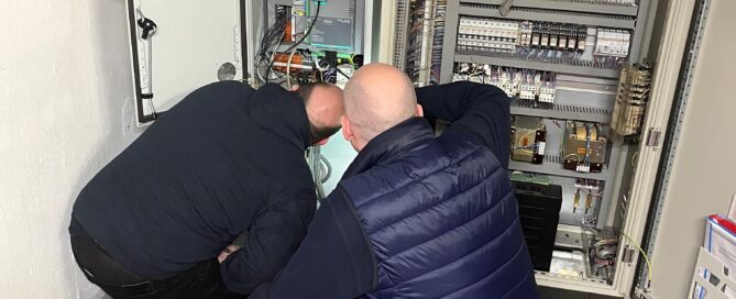 Two lift engineers crouching to look at lift controllers
