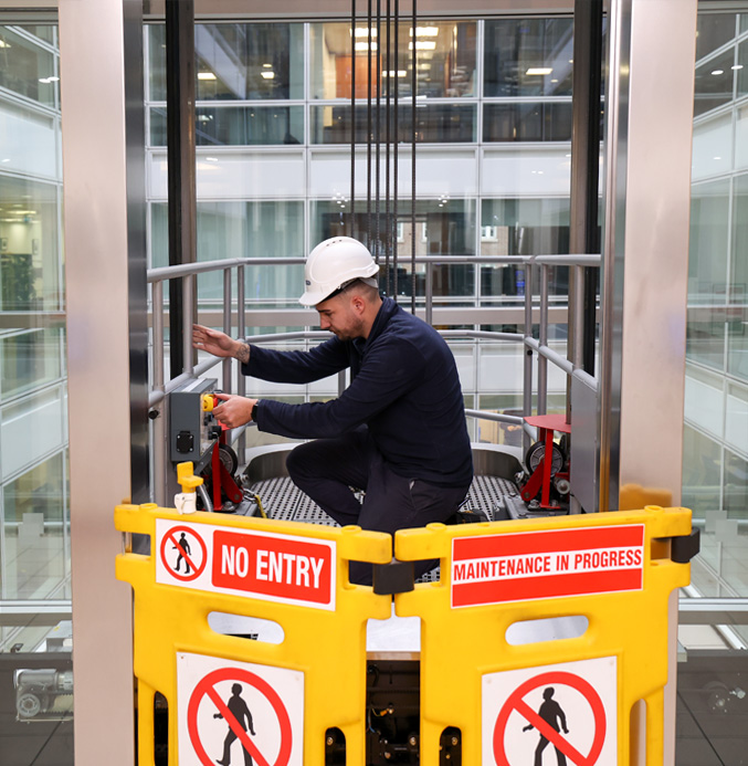 Apex engineer maintaining a lift with warning signs in front of him